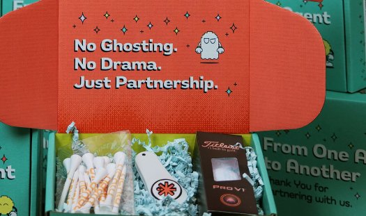 Nexio partner kit box reading “No Ghosting. No Drama. Just Partnership.” with golf tees, a divot tool and a Titleist Pro V1 ball inside